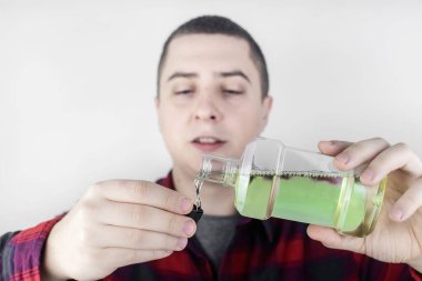 Tuvalette ağız gargarası kullanan bir adamın yakın çekimi. Diş bakımı konsepti. Dişlerini fırçaladıktan sonra prosedür. Antibakteriyel ağız sıvısı. Döküyor, duruluyor ve tükürüyor. Adam aynaya bak.