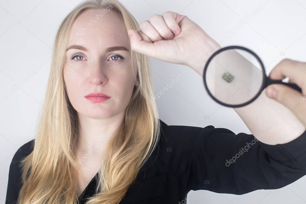 The woman shows his hand with a chip implanted which is studied with a magnifying glass. The concept of chipping and implantation of electronic technologies. Cybernetics and the nanofuture. Cyberpunk