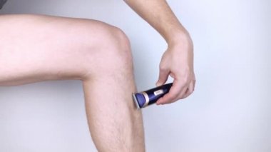 Beyaz arka planda bir adam bacaklarını tıraş eder. Kıllı bacaklar ve onlarla ilgilenmek. Cinsiyet eşitliği kavramı. Köpüğü, jileti ve pürüzsüz bir bacakta tıraş edilmiş saçı gösteren yakın plan bir fotoğraf..