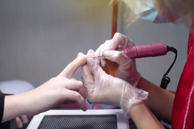 Manikürcü kadının tırnaklarını elektrikli bir dosya ile inceliyor. Güzellik salonunda profesyonel bakım. Manikür işlemi. Bir uzmanın çalışmasına yakın çekim.