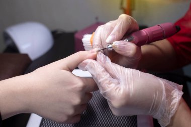 Manikürcü kadının tırnaklarını elektrikli bir dosya ile inceliyor. Güzellik salonunda profesyonel bakım. Manikür işlemi. Bir uzmanın çalışmasına yakın çekim.