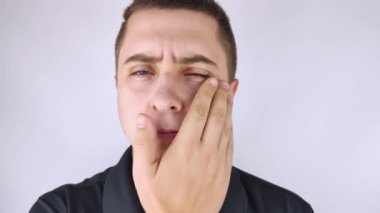 Bir adam aynanın önünde duruyor ve göz kapağının üst kısmındaki iltihabı görüyor. Gözlerinin etrafındaki cilt kırmızısı ve kanama..