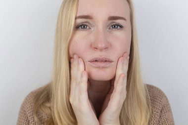 Bir kadın dudaklarındaki kuru deriyi inceliyor. Soyulma, kabalaşma, rahatsızlık, cilt hassasiyeti. Dermatolog ya da kozmetikçinin randevusundaki hasta. Kuru deri parçalarının yakın çekimi