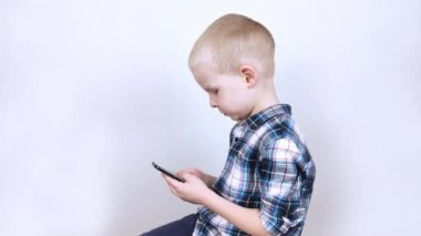 Beyaz arka plandaki bir video oyununda akıllı bir telefonla oynayan bir çocuk. Video oyunlarına ve cep telefonlarına çocuk bağımlılığı kavramı. Aletlere güçlü bir bağlılık ve oyunları bitirme isteksizliği. 