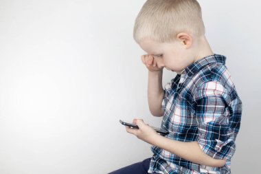 Beyaz arka plandaki bir video oyununda akıllı bir telefonla oynayan bir çocuk. Video oyunlarına ve cep telefonlarına çocuk bağımlılığı kavramı. Aletlere güçlü bir bağlılık ve oyunları bitirme isteksizliği.