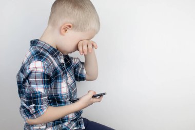 Beyaz arka plandaki bir video oyununda akıllı bir telefonla oynayan bir çocuk. Video oyunlarına ve cep telefonlarına çocuk bağımlılığı kavramı. Aletlere güçlü bir bağlılık ve oyunları bitirme isteksizliği.