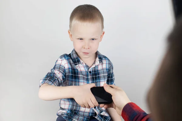 Dad tries to take the child\'s phone, on which he plays for a long time. The guy does not give up his smartphone and behaves aggressively. Child addiction to mobile phones and video games.