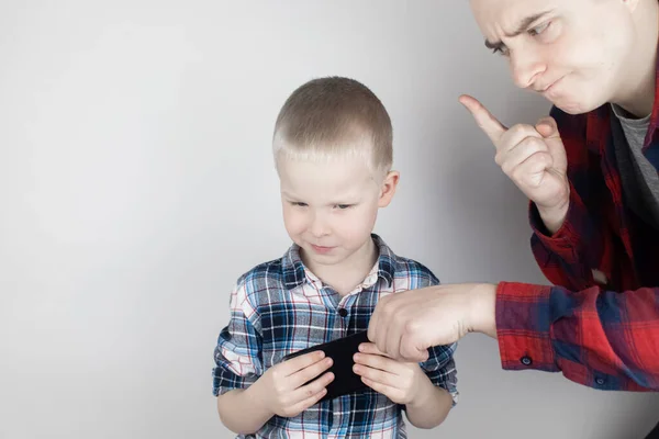 Dad tries to take the child\'s phone, on which he plays for a long time. The guy does not give up his smartphone and behaves aggressively. Child addiction to mobile phones and video games.