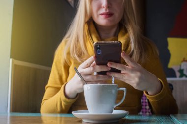 Blogcu kız bir kafede oturur ve akıllı telefondan kapuçino köpüğü atar. Sosyal ağlarda, video bloglarında ve fotoğraf bloglarında çalışıyorum. İnternet içeriği oluşturma ve gıda fotoğrafçılığı kavramı.