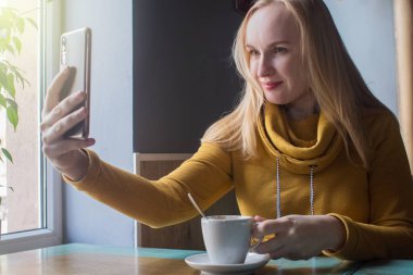 Blogcu kız bir kafede oturur ve akıllı telefondan kapuçino köpüğü atar. Sosyal ağlarda, video bloglarında ve fotoğraf bloglarında çalışıyorum. İnternet içeriği oluşturma ve gıda fotoğrafçılığı kavramı.