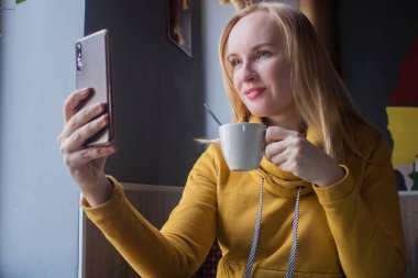 Blogcu kız bir kafede oturur ve akıllı telefondan kapuçino köpüğü atar. Sosyal ağlarda, video bloglarında ve fotoğraf bloglarında çalışıyorum. İnternet içeriği oluşturma ve gıda fotoğrafçılığı kavramı.