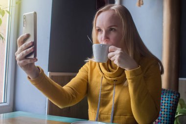 Blogcu kız bir kafede oturur ve akıllı telefondan kapuçino köpüğü atar. Sosyal ağlarda, video bloglarında ve fotoğraf bloglarında çalışıyorum. İnternet içeriği oluşturma ve gıda fotoğrafçılığı kavramı.