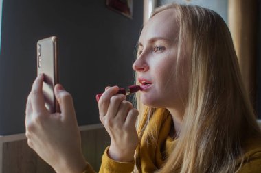 Kız bir kafede dudaklarını boyuyor. Yemekten sonra makyajını yapan tatlı bir kızın yakın çekimi. Kadın çok renkli bir çerçevede bir ayna tutuyor. Kişisel bakım ve makyaj konsepti