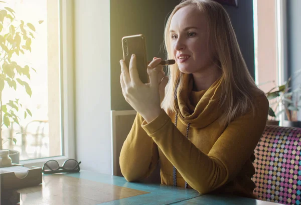 Kız bir kafede dudaklarını boyuyor. Yemekten sonra makyajını yapan tatlı bir kızın yakın çekimi. Kadın çok renkli bir çerçevede bir ayna tutuyor. Kişisel bakım ve makyaj konsepti