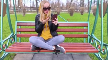 Blogcu kız parkta salıncakta oturuyor ve içerik yaratıyor. Sosyal ağlarda, video bloglarında ve fotoğraf bloglarında çalışıyorum. İnternet içeriği, eğitim ve çevrimiçi tanıtım kavramı