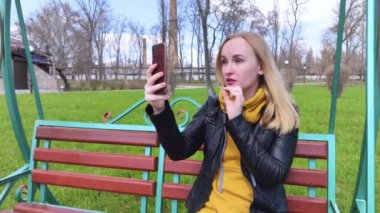 Blogcu kız parkta salıncakta oturuyor ve içerik yaratıyor. Sosyal ağlarda, video bloglarında ve fotoğraf bloglarında çalışıyorum. İnternet içeriği, eğitim ve çevrimiçi tanıtım kavramı