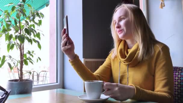 ブロガーの女の子はカフェに座って スマートフォンでカプチーノ泡を撮影します ソーシャルネットワーク ビデオブログや写真ブログで仕事をします インターネットコンテンツ制作と食写真のコンセプト — ストック動画