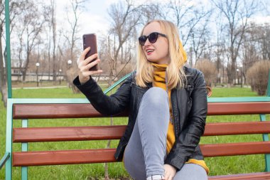 Blogcu kız parkta salıncakta oturuyor ve içerik yaratıyor. Sosyal ağlarda, video bloglarında ve fotoğraf bloglarında çalışıyorum. İnternet içeriği, eğitim ve çevrimiçi tanıtım kavramı