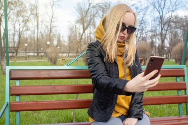 Blogcu kız parkta salıncakta oturuyor ve içerik yaratıyor. Sosyal ağlarda, video bloglarında ve fotoğraf bloglarında çalışıyorum. İnternet içeriği, eğitim ve çevrimiçi tanıtım kavramı