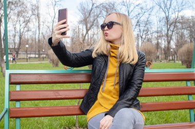 Blogcu kız parkta salıncakta oturuyor ve içerik yaratıyor. Sosyal ağlarda, video bloglarında ve fotoğraf bloglarında çalışıyorum. İnternet içeriği, eğitim ve çevrimiçi tanıtım kavramı