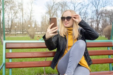 Blogcu kız parkta salıncakta oturuyor ve içerik yaratıyor. Sosyal ağlarda, video bloglarında ve fotoğraf bloglarında çalışıyorum. İnternet içeriği, eğitim ve çevrimiçi tanıtım kavramı