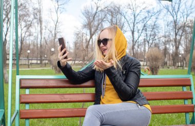 Blogcu kız parkta salıncakta oturuyor ve içerik yaratıyor. Sosyal ağlarda, video bloglarında ve fotoğraf bloglarında çalışıyorum. İnternet içeriği, eğitim ve çevrimiçi tanıtım kavramı