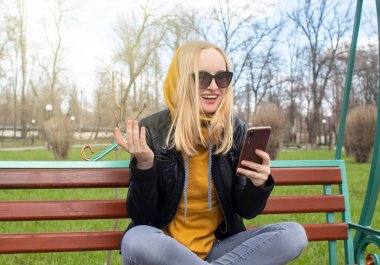 Blogcu kız parkta salıncakta oturuyor ve içerik yaratıyor. Sosyal ağlarda, video bloglarında ve fotoğraf bloglarında çalışıyorum. İnternet içeriği, eğitim ve çevrimiçi tanıtım kavramı
