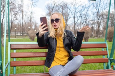 Blogcu kız parkta salıncakta oturuyor ve içerik yaratıyor. Sosyal ağlarda, video bloglarında ve fotoğraf bloglarında çalışıyorum. İnternet içeriği, eğitim ve çevrimiçi tanıtım kavramı