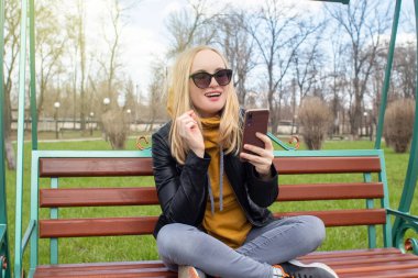 Blogcu kız parkta salıncakta oturuyor ve içerik yaratıyor. Sosyal ağlarda, video bloglarında ve fotoğraf bloglarında çalışıyorum. İnternet içeriği, eğitim ve çevrimiçi tanıtım kavramı
