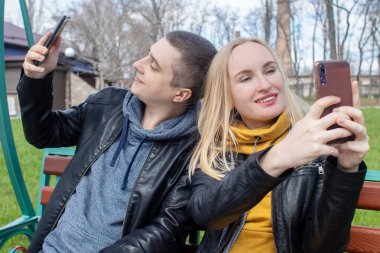 Karı koca parkta salıncakta sallanırken selfie çekiyorlar. Mutlu çift kendi fotoğraflarını çekiyor. Mutlu aile kavramı, poz vermek ve anı yakalamak..