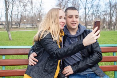 Karı koca parkta salıncakta sallanırken selfie çekiyorlar. Mutlu çift kendi fotoğraflarını çekiyor. Mutlu aile kavramı, poz vermek ve anı yakalamak..