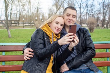 Karı koca parkta salıncakta sallanırken selfie çekiyorlar. Mutlu çift kendi fotoğraflarını çekiyor. Mutlu aile kavramı, poz vermek ve anı yakalamak..
