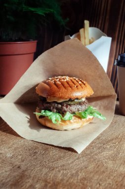 Kağıt ambalajlı hamburger. Yakın plan. Fast food restoranında yemek. Etli ve sebzeli hamburger malzemelerinin makro fotoğrafı.