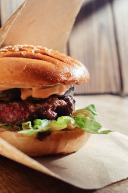 Kağıt ambalajlı hamburger. Yakın plan. Fast food restoranında yemek. Etli ve sebzeli hamburger malzemelerinin makro fotoğrafı.