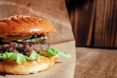 Kağıt ambalajlı hamburger. Yakın plan. Fast food restoranında yemek. Etli ve sebzeli hamburger malzemelerinin makro fotoğrafı.