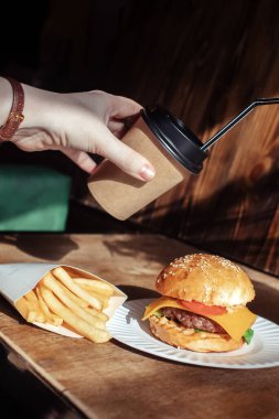 Kağıt ambalajda hamburger, kahve ve yakın plan patates kızartması. Fast food restoranında yemek. Etli ve sebzeli bir hamburger, patates kızartması ve kahve. Fast food seti