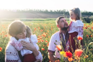 Ulusal Slav kostümü giymiş haşhaş tarlasında bir aile. Annem, babam ve işlemeli gömlekli ikiz kızlar güneşli bir günde eğleniyorlar. Mutlu bir çocukluk, tarih ve atalarımızla birliktelik kavramı