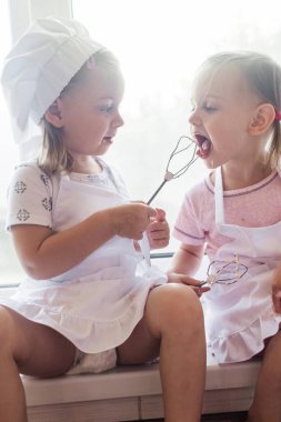 Çocuklar mutfakta aileleriyle yemek pişiriyor. Bütün aile için ev yapımı kek, pasta ya da kurabiye yapıyorum. Mutlu çocukluk kavramı. Mutfak önlükleri ve şef şapkaları takan küçük ikiz kardeşler.