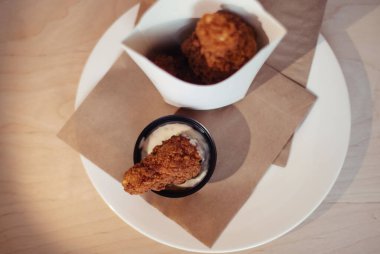 Hamurda kızartılmış tavuk kanadı yakın çekim. Bir fast food restoranında masanın üzerinde karton bir tavuk ve sos kutusu var. Güneş ışınları, yiyecekleri tutan kızın eline çok güzel düşer.