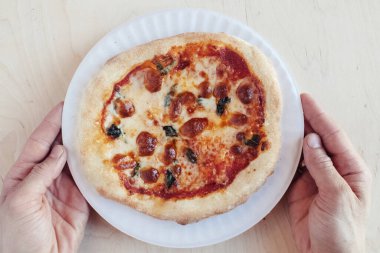 Tek kullanımlık tabakta mini bir pizzanın yakın çekimi. Fast food Cafe 'nin en iyi yemek manzarası. Fotoğrafta mozarella peyniri, domates, zeytin ve çeşitli sosisler var. Bir kişilik yemek.
