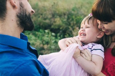 Üç kişilik mutlu bir aile sahada eğleniyor ve eğleniyor. Baba, anne ve kızı bir çiçek çayırında oynuyorlar ve eğleniyorlar. Bir çocukla mutlu aile kavramı. Samimi gülüşler ve kahkahalar
