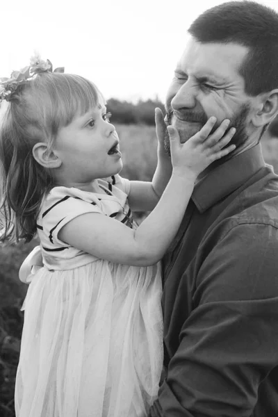 Dad and daughter play together on the flower field. Happy and caring father is having fun with his daughter. Dad pays attention to his child. Bearded man and little girl with flowers in their hair