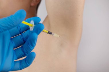 Klinikte hiperhidrozun tedavisi için koltukaltına botoks yapılan bir adam. Artan terleme, anhidroz ya da arızalı bezlerle ilgili sorunların tedavisi. Kozmetolojide Botulinum toksini