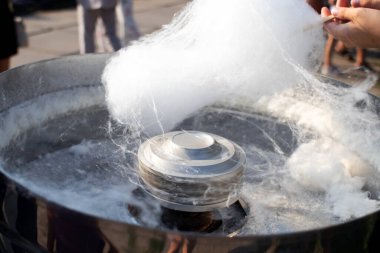 Pamuk helva yapan bir adamın yakın çekimi. Tahta sopa, tatlı örümcek ağının iplerini saracak. Tatlı bulut ve eritilmiş ikram makinesi. Sokak yemekleri ve karnaval lezzeti kavramı..