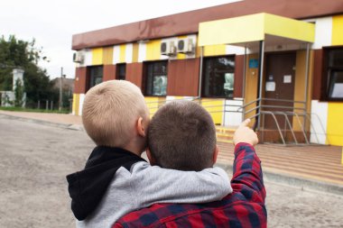 Baba, oğlunu doktora götürüyor. Standart bir hastane binasının zemininde baba ve oğul muayene için hazırlanıyor. Tek bir ebeveynin çocuğunu okula ya da anaokuluna hazırlaması kavramı