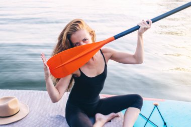 Yemek masasında yüzen bir kızın yakın çekimi. Su sporları, rahatlama ve kendini kaptırma kavramı. Yalnız bir kadın su ve rıhtımın arka planında tek başına..