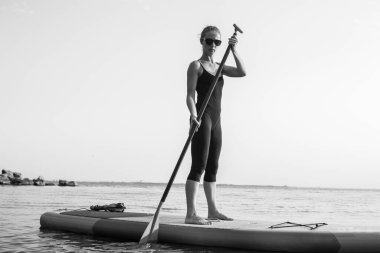 Yemek masasında yüzen bir kızın yakın çekimi. Su sporları, rahatlama ve kendini kaptırma kavramı. Yalnız bir kadın su ve rıhtımın arka planında tek başına..
