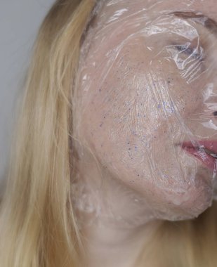 Kozmetik alanında mikroplastikler. Bir kadın cildine bakım kremi sürmüş, şimdi plastik parçacıklar ve mikroboncuklarla kaplanmış. Kozmetik zehirlenmesi konsepti