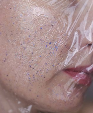 Kozmetik alanında mikroplastikler. Bir kadın cildine bakım kremi sürmüş, şimdi plastik parçacıklar ve mikroboncuklarla kaplanmış. Kozmetik zehirlenmesi konsepti