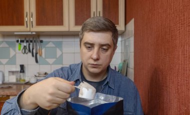 Adam mutfakta protein içeceği hazırlıyor. Tozu fitness, iyileşme ve kas sağlığı için karıştırıcıya dönüştürüyor..